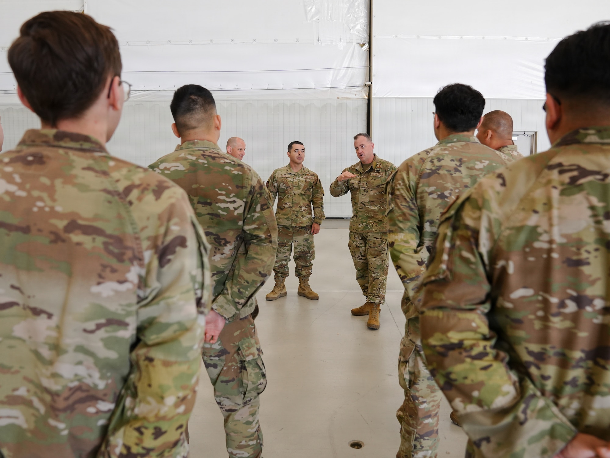 A man in a military uniform addresses a hangar full of people in military uniform.