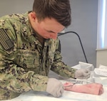 PATUXENT RIVER, Md. — Hospitalman Apprentice Branden Slaughterback, from Navy Medicine Readiness and Training Command (NMRTC) Detachment Indian Head, practices wound closure techniques on a pig's foot during a hands-on suture lab at NMRTC Patuxent River. The training, which brought together corpsmen from across the National Capital Region, was designed to enhance life-saving skills and ensure a ready medical force.