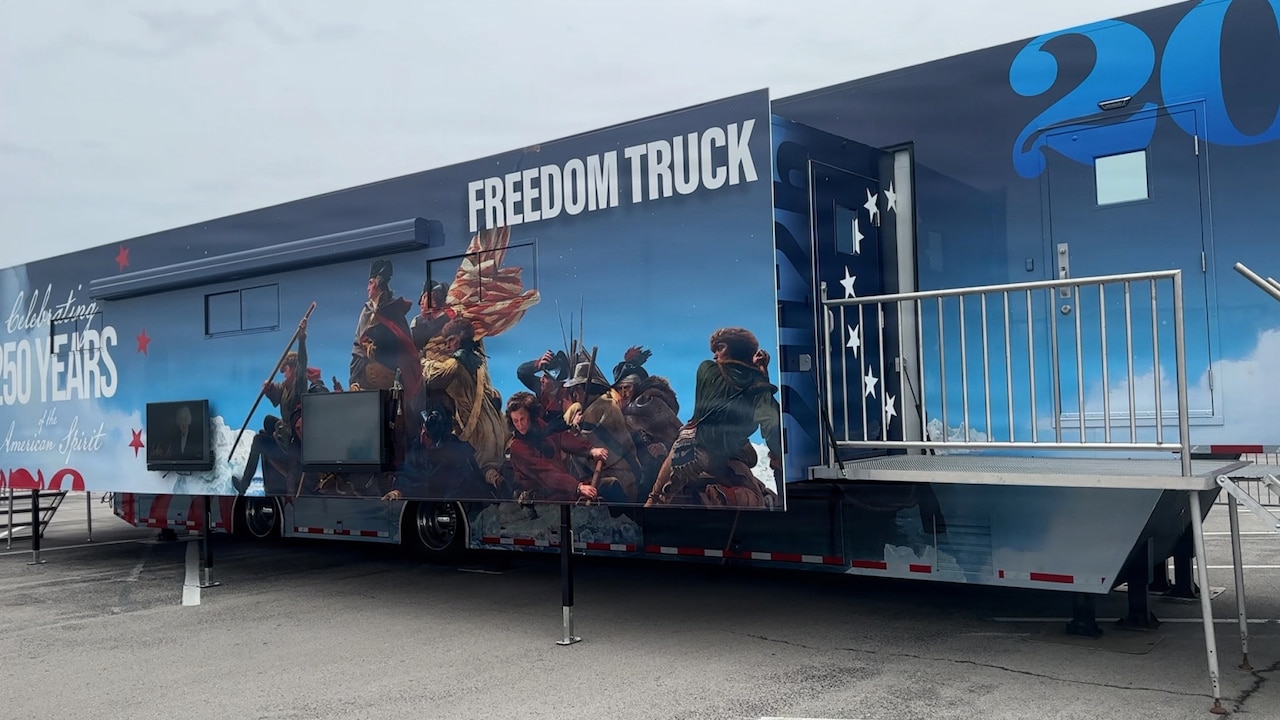 A trailer with “Freedom Truck” written on the side is sitting in a parking lot. A historic battle scene is painted on the side of the trailer.
