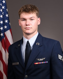 Official photo of Senior Airman Logan Grindstaff with flag in backround.