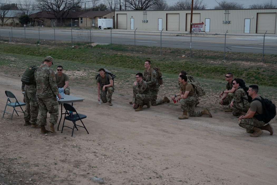 Participants take a knee at station 5 during the inaugural Noncommissioned Officer Ruck March at Goodfellow Air Force Base, Texas, March 5, 2026. Volunteers manned stations along the trail for participants to learn about what it means to be a NCO and how to handle certain situations as a NCO. (U.S. Air Force photo by Senior Airman Brian Lummus)