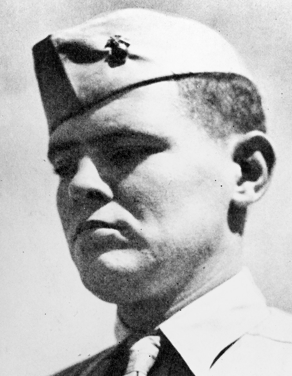 A man in a military cap looks stoic while looking toward the ground.