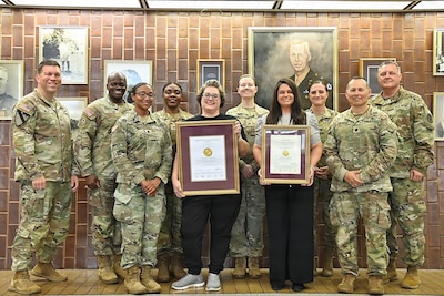 Ten people pose in front of a memorial wall honoring two with awards.