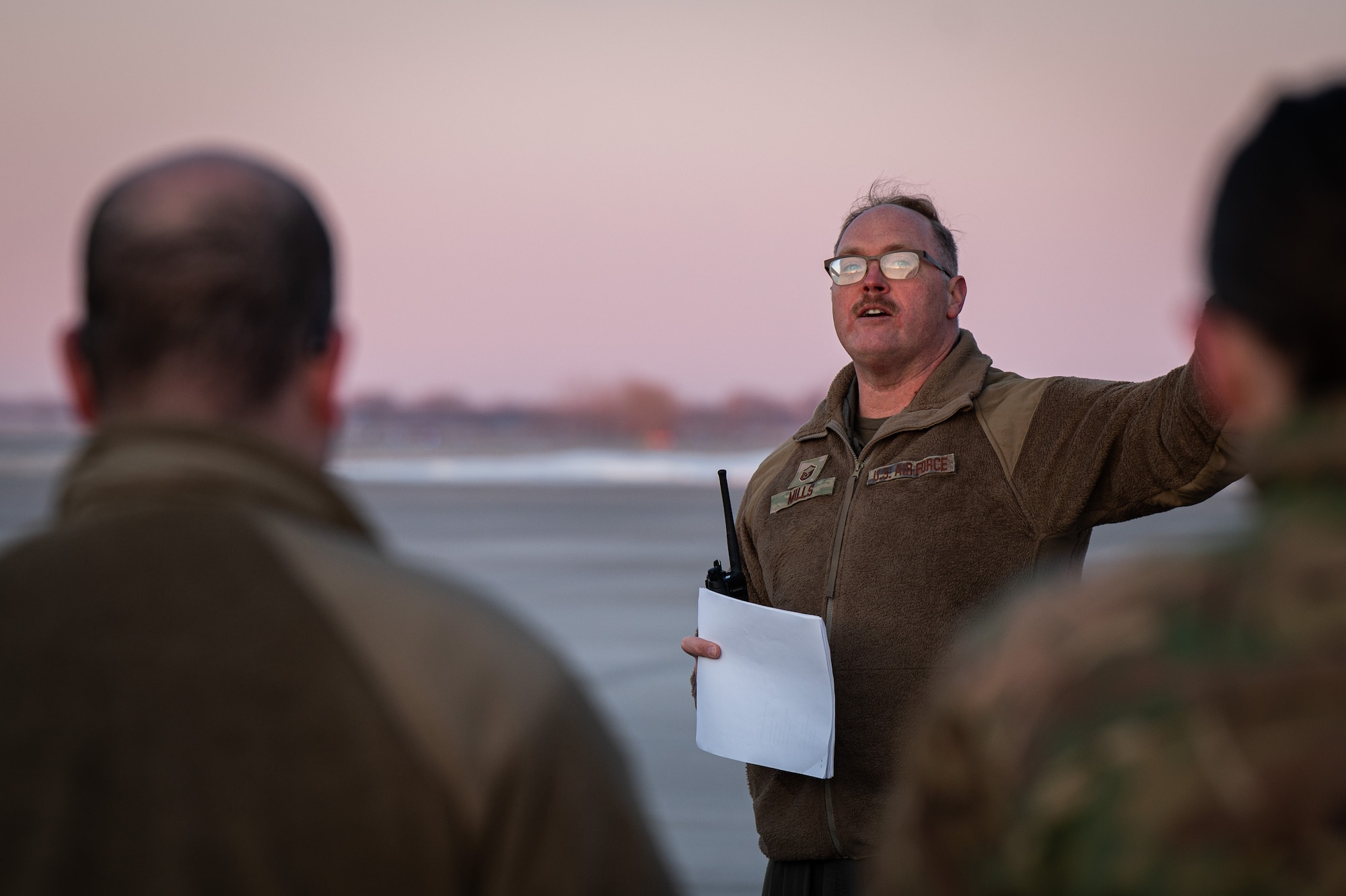 A photo of a man standing and speaking to a group of people outside.