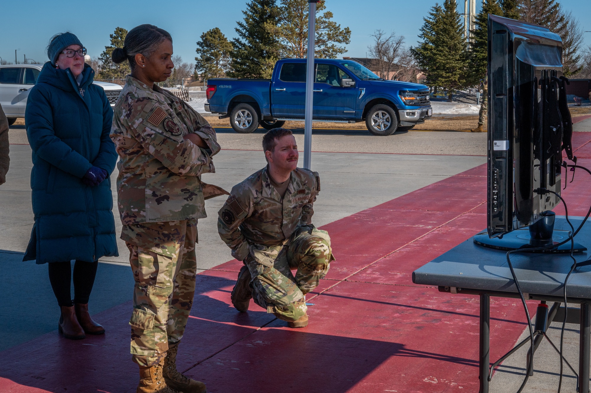 A photo of three people standing outside looking at a television screen.