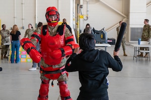 A U.S. Airman assigned to the 7th Security Forces Squadron demonstrates the red man full body protective suit to safely simulate realistic combat scenarios  with a student during a career fair at Dyess Air Force Base, Texas, Feb. 26, 2026. Students participated in demonstrations and viewed exhibits from 38 career fields during the event. (U.S. Air Force photo by Airman 1st Class William Neal)