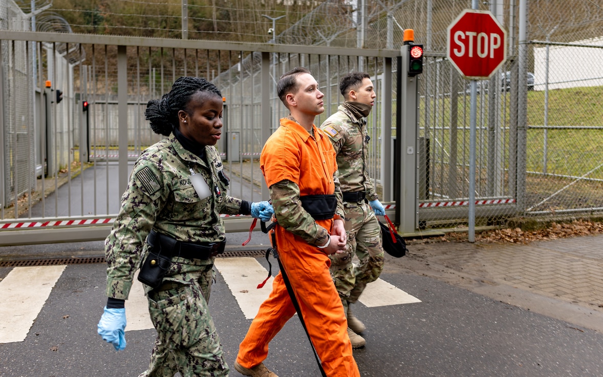 U.S. Navy Petty Officer 2nd Class Ella Koudaya and U.S. Army Sgt. Norberto Fernandez, corrections and detention specialists assigned to United States Army Correctional Activity–Europe, 18th Military Police Brigade, escort a simulated prisoner to a new location during a prisoner relocation exercise at the correctional facility on U.S. Army Garrison Sembach.