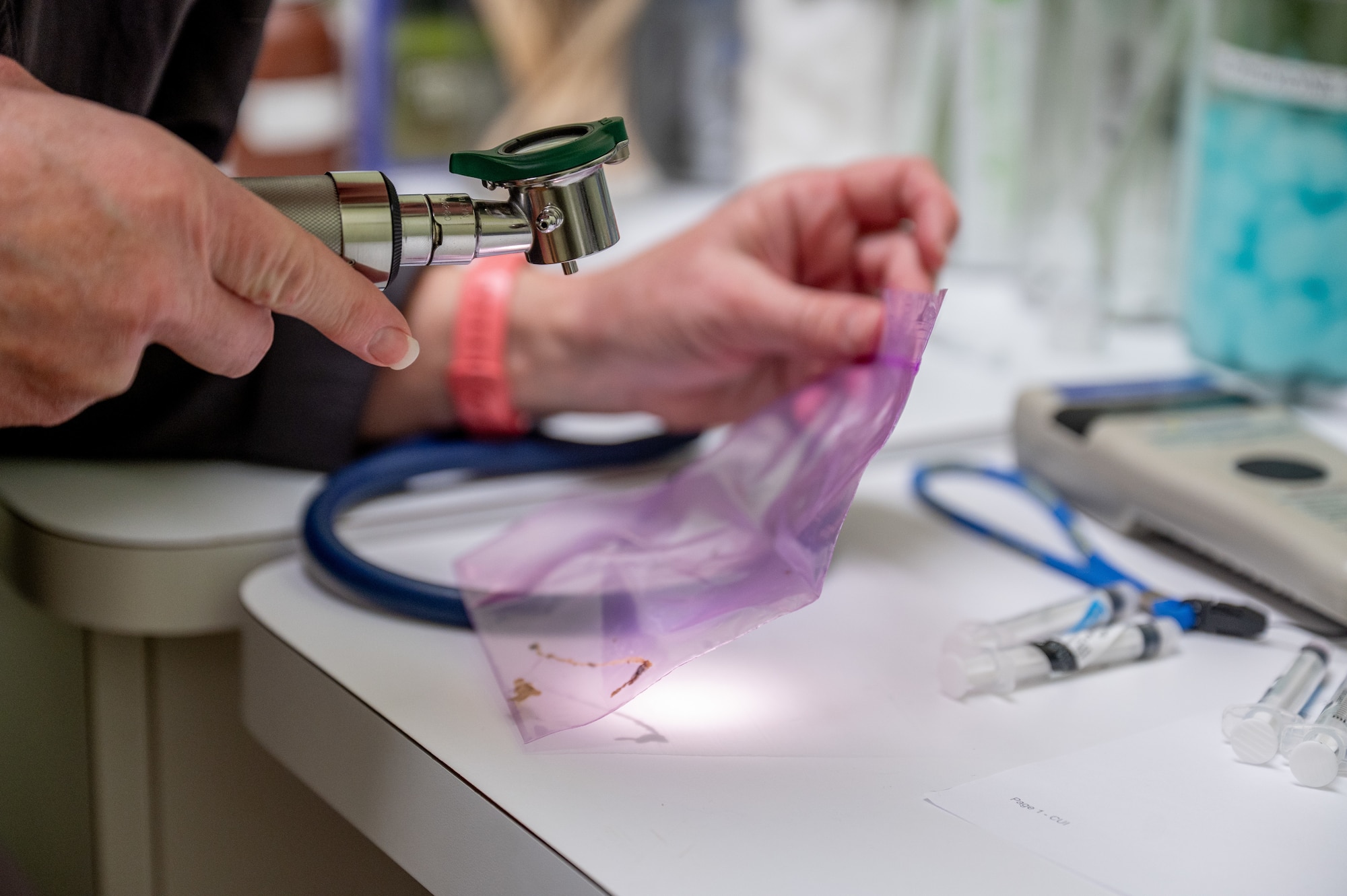A Maxwell Air Force Base Veterinarian uses a microscope to inspect an item in a plastic bag.