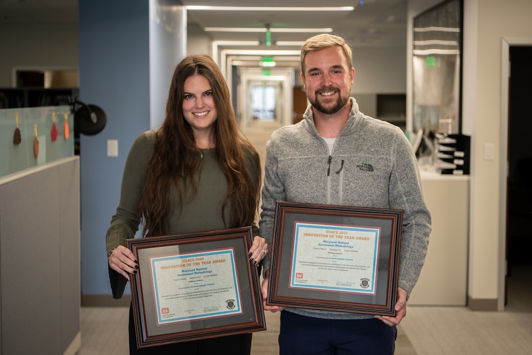 A smiling man and woman stand in an office hallway, each holding a framed "Innovation of the Year" award certificate.