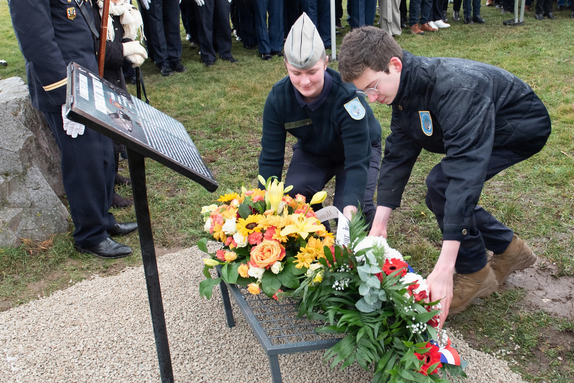Photo shows two French residents placing a bouquet of flowers on a memorial during a ceremony.