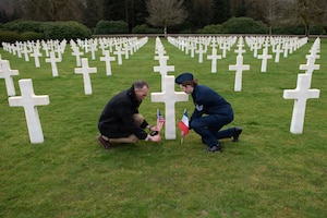 Photo shows a French citizen and a U.S. Airmen planting their national flags at a grave at a cemetery.