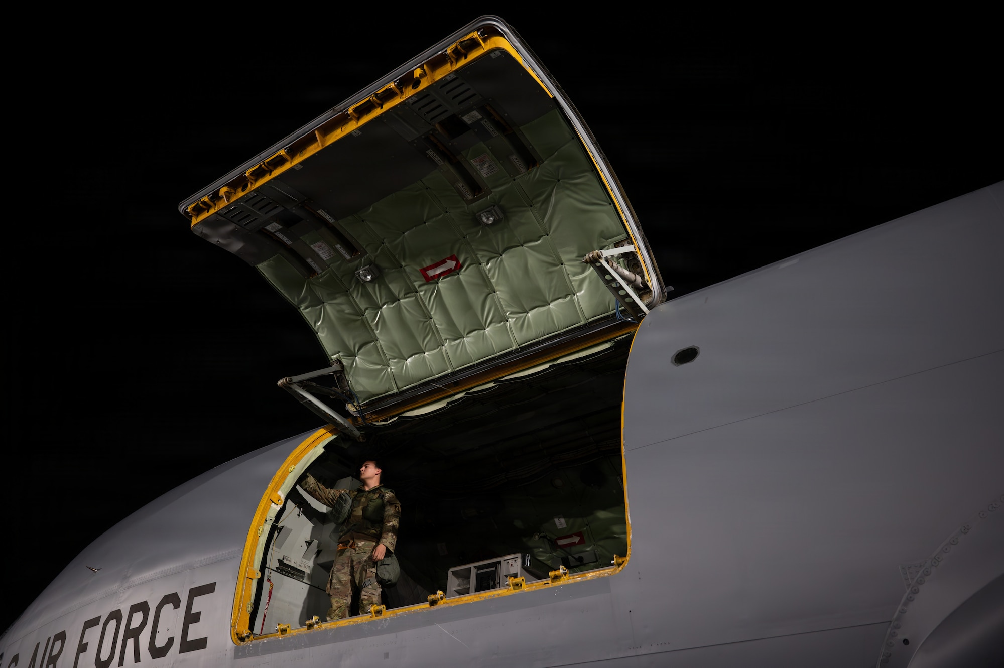 An Airman stands at the open hatch of an aircraft.