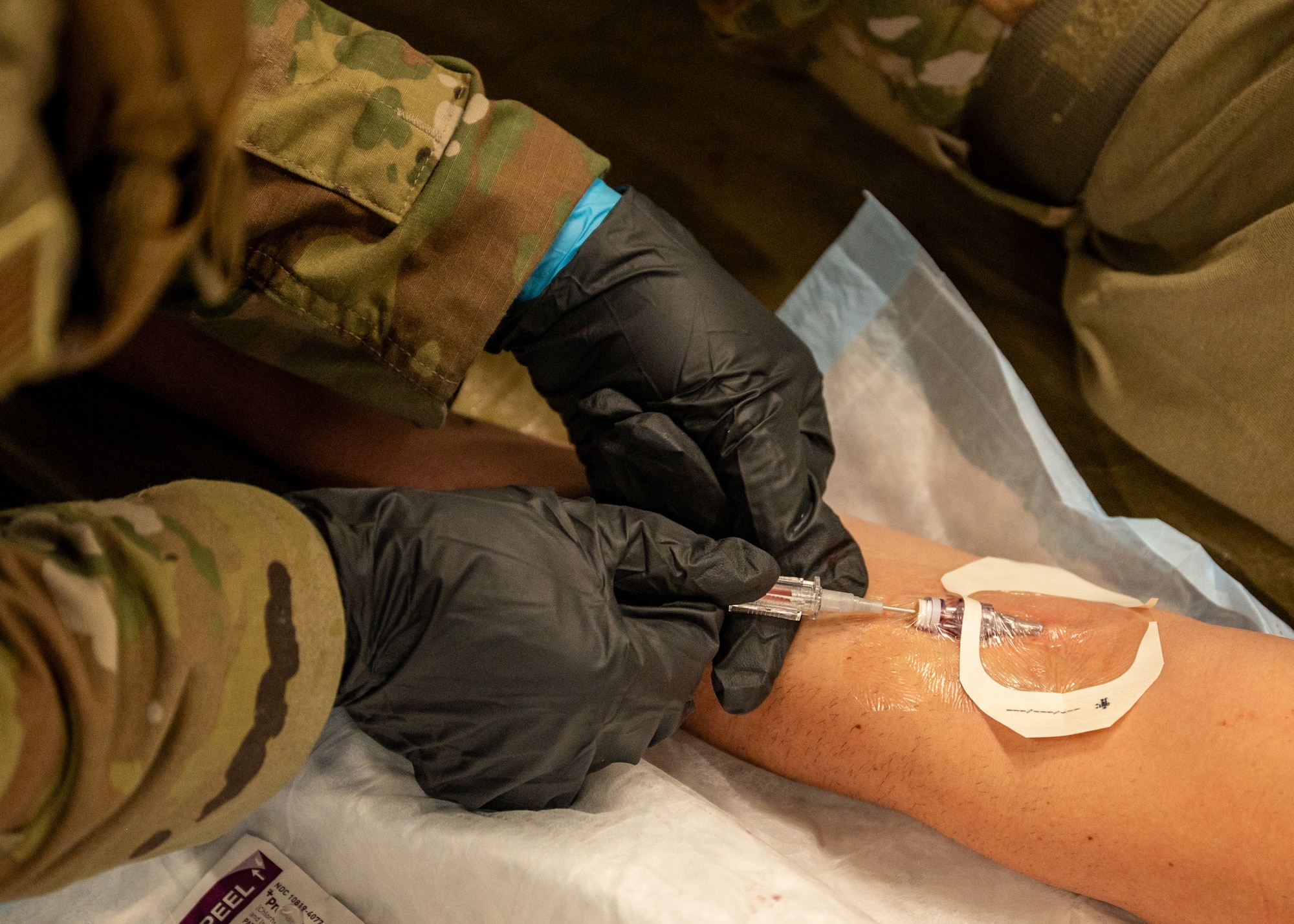 A military medic inserts an IV into another service member's arm.
