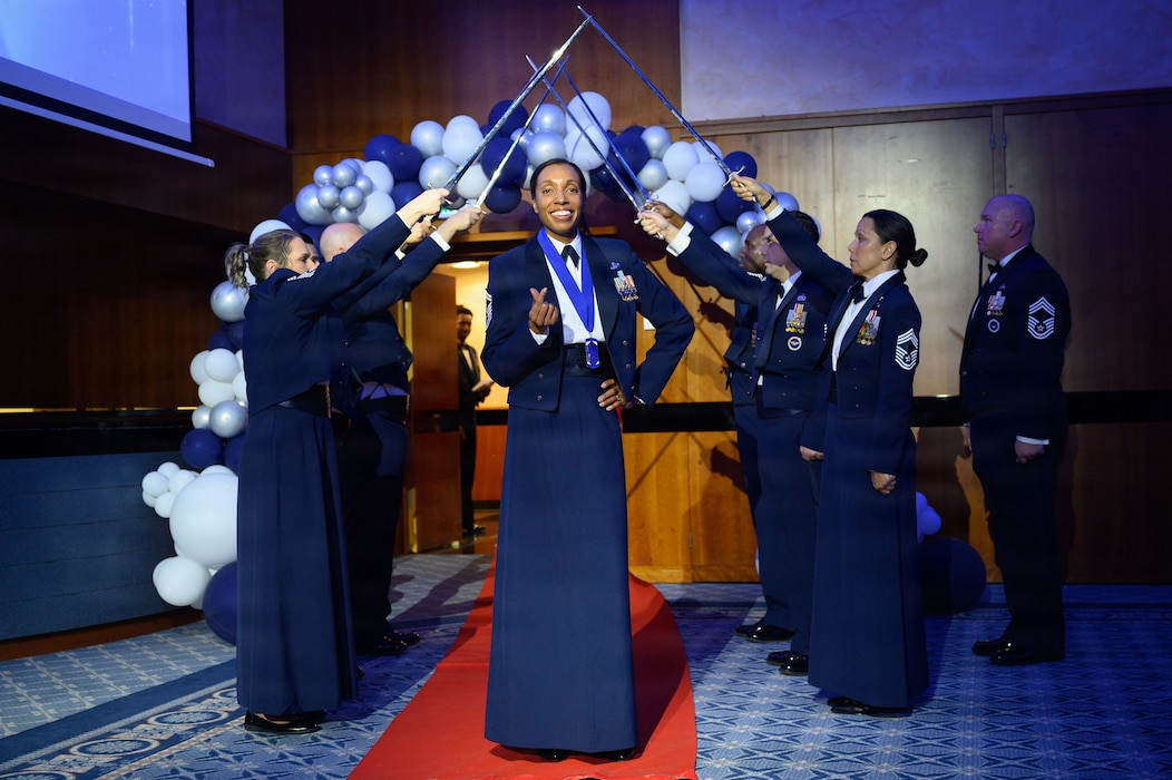 A person being promoted to Chief Master Sgt. stands at the end of an arch of sabers.