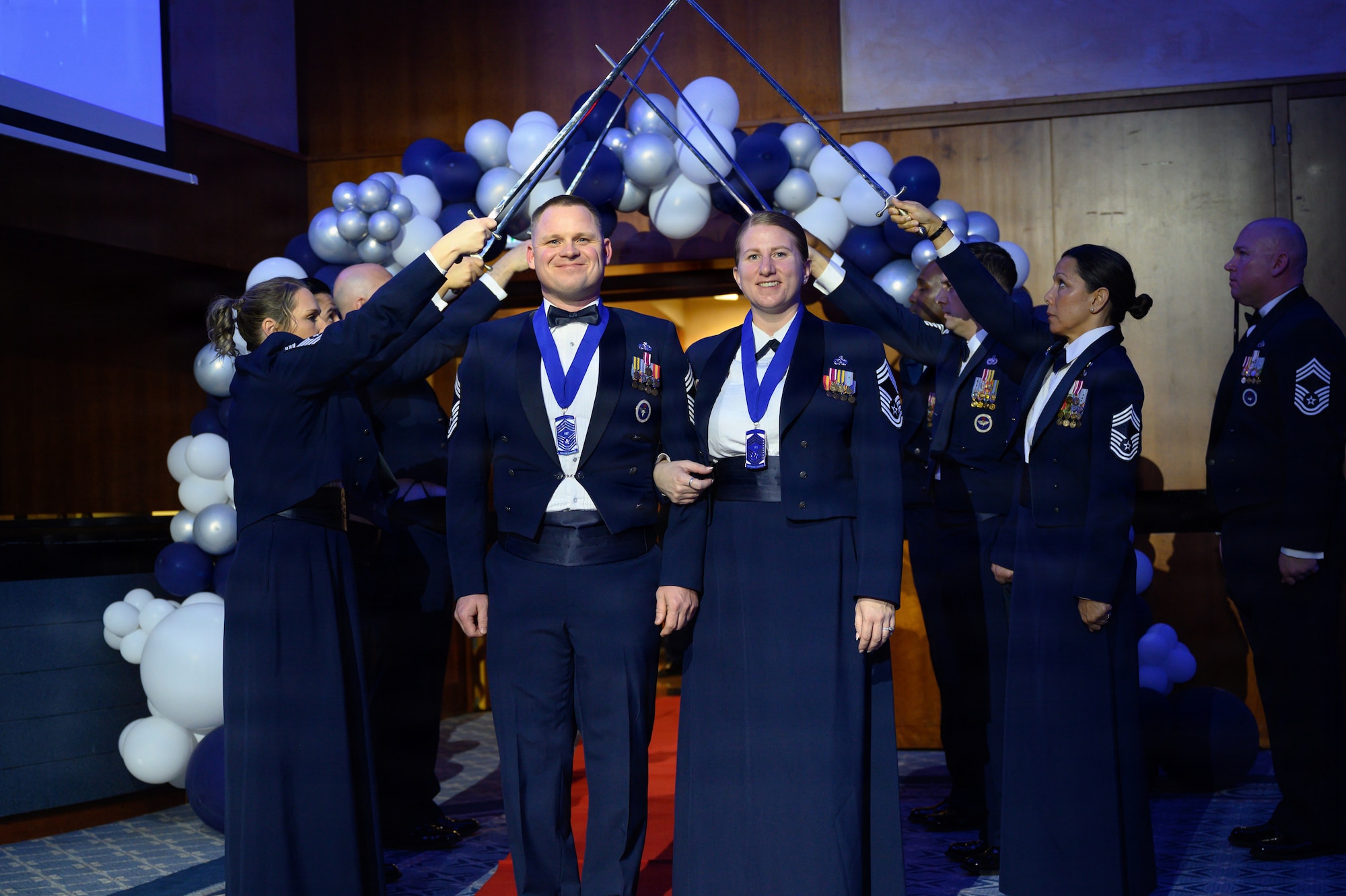 A married couple who are both being celebrated for their promotions to Chief Master Sgt. pose at the end of an arch of sabers.