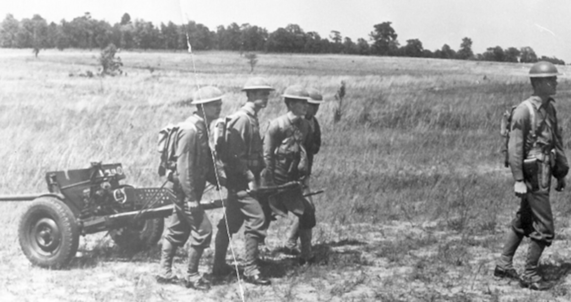 A soldier walks in front of three men pulling antitank equipment behind them
