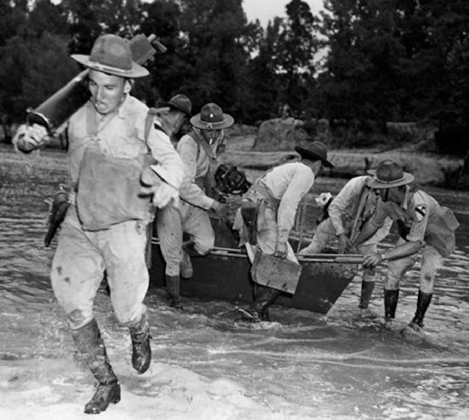 A machine gun squad pulls a boat through shallow river waters