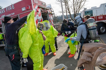 Clackamas and Gresham firefighters prepare to work in a contaminated zone by donning protective chemical suits during response procedures in an Air Monitoring Exercise on Feb. 26, 2026, in Clackamas, Oregon.
