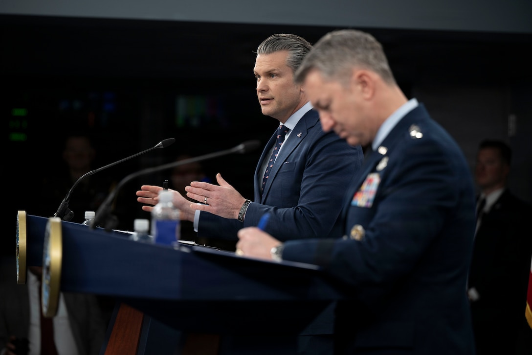 Secretary of War Pete Hegseth speaks at a lectern beside Air Force Gen. Dan Caine at another one.