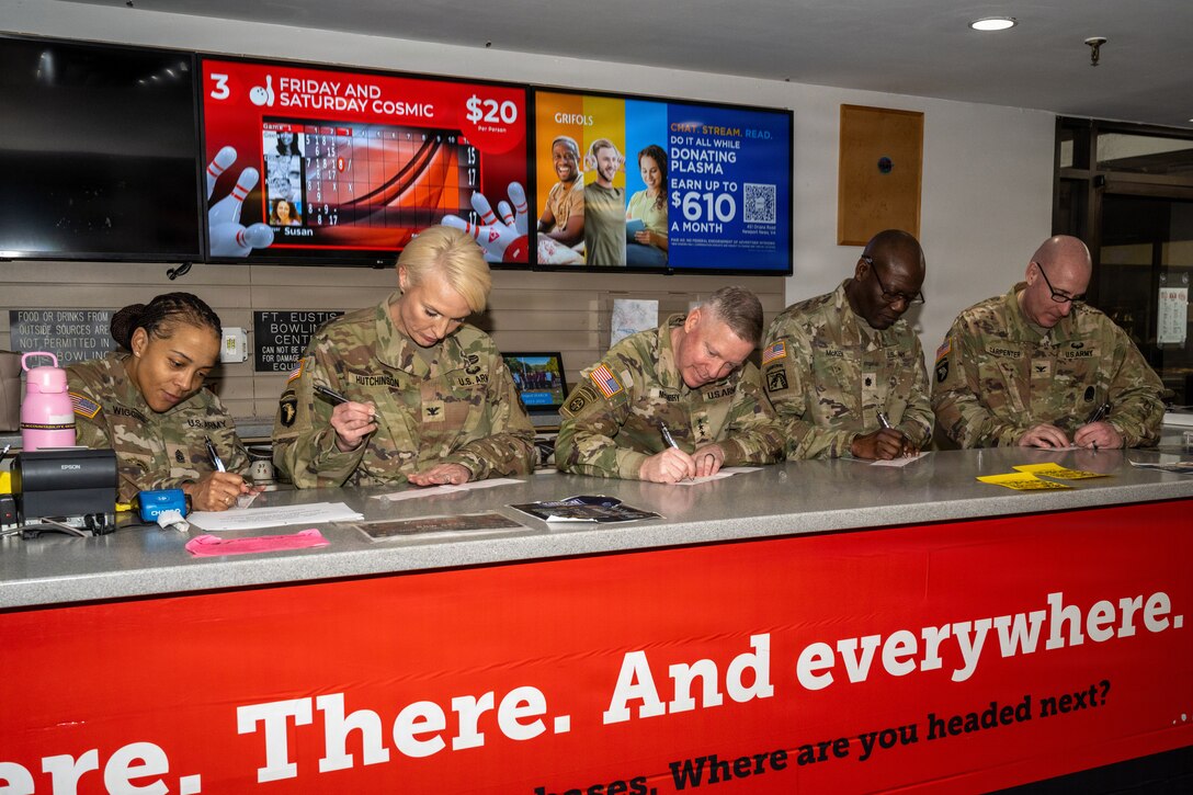 Two women and three men stand beside each other while signing checks.