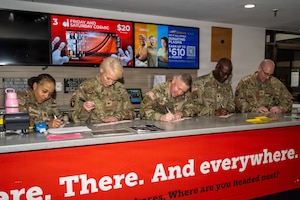 Two women and three men stand beside each other while signing checks.