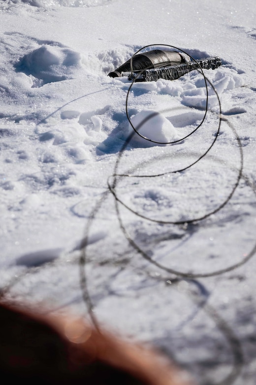 A military warhead sits on a snow-covered ground next to a block of a military explosive.