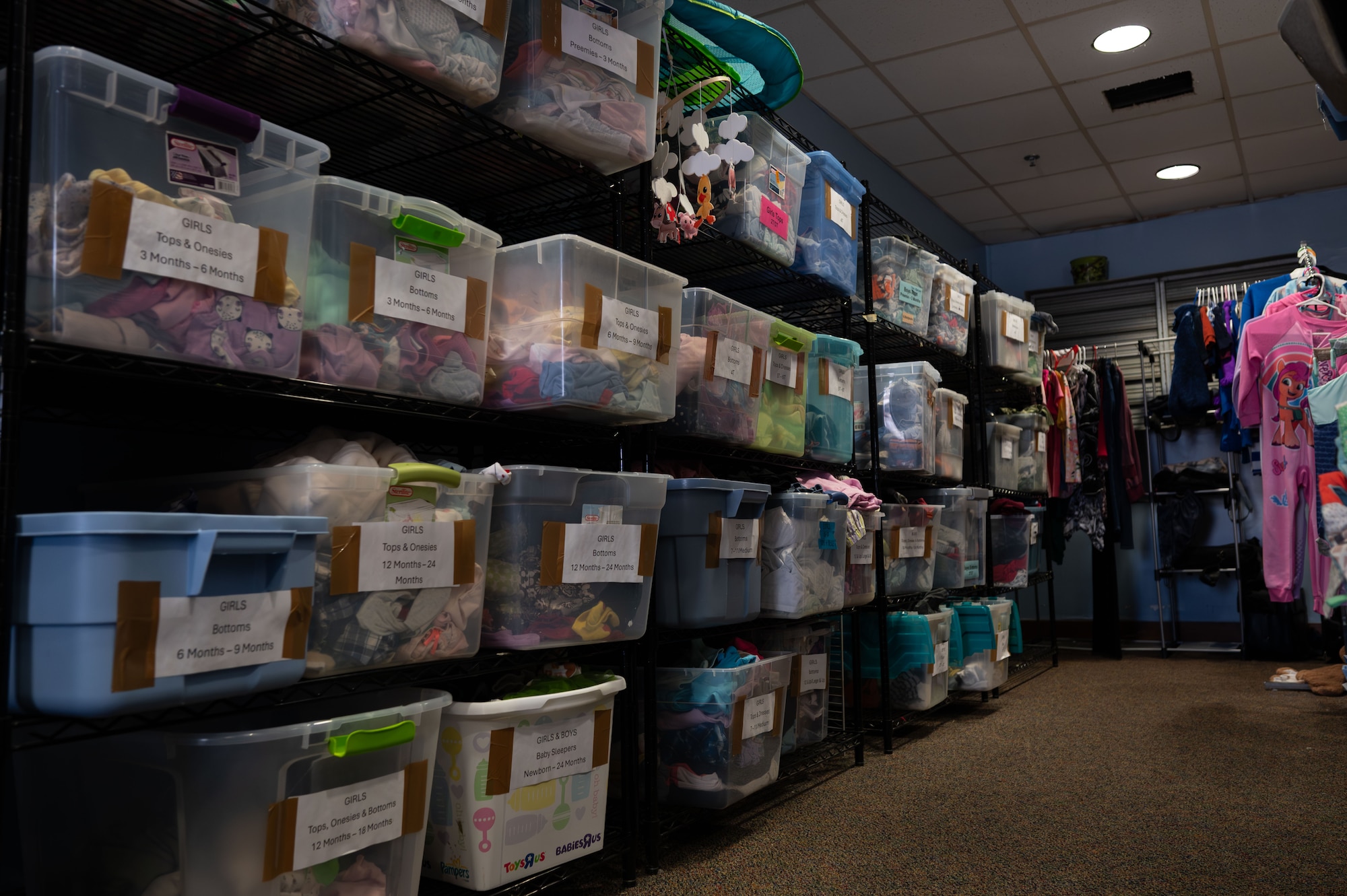 Tubs of children’s clothes are stacked on shelves at the Airmen’s Attic on Dover Air Force Base, Delaware, March 2, 2026. The Airmen’s Attic is not only for adults; they also supply children's clothing, books and toys. (U.S. Air Force photo by Airman 1st Class Liberty Kuhn)