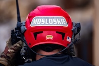 A red helmet is being worn by someone with a walkie talkie in their hand, and on the back of the help is the word Mosloskie.