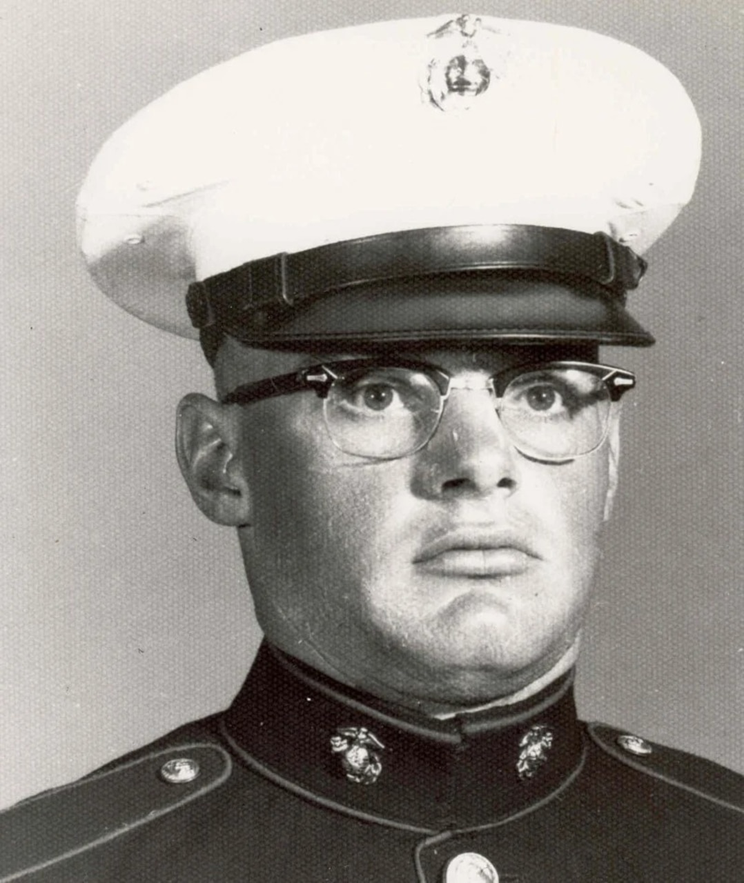 A man wearing a cap and military dress uniform poses stoically for a photo.