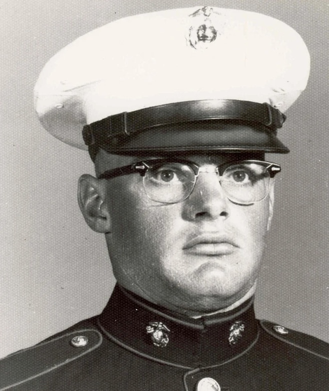 A man wearing a cap and military dress uniform poses stoically for a photo.
