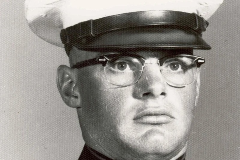 A man wearing a cap and military dress uniform poses stoically for a photo.