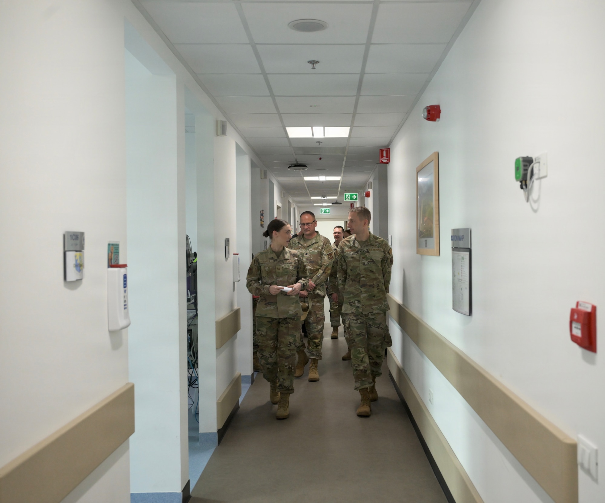 Two Air Force service members walk down a hallway speaking with each other.