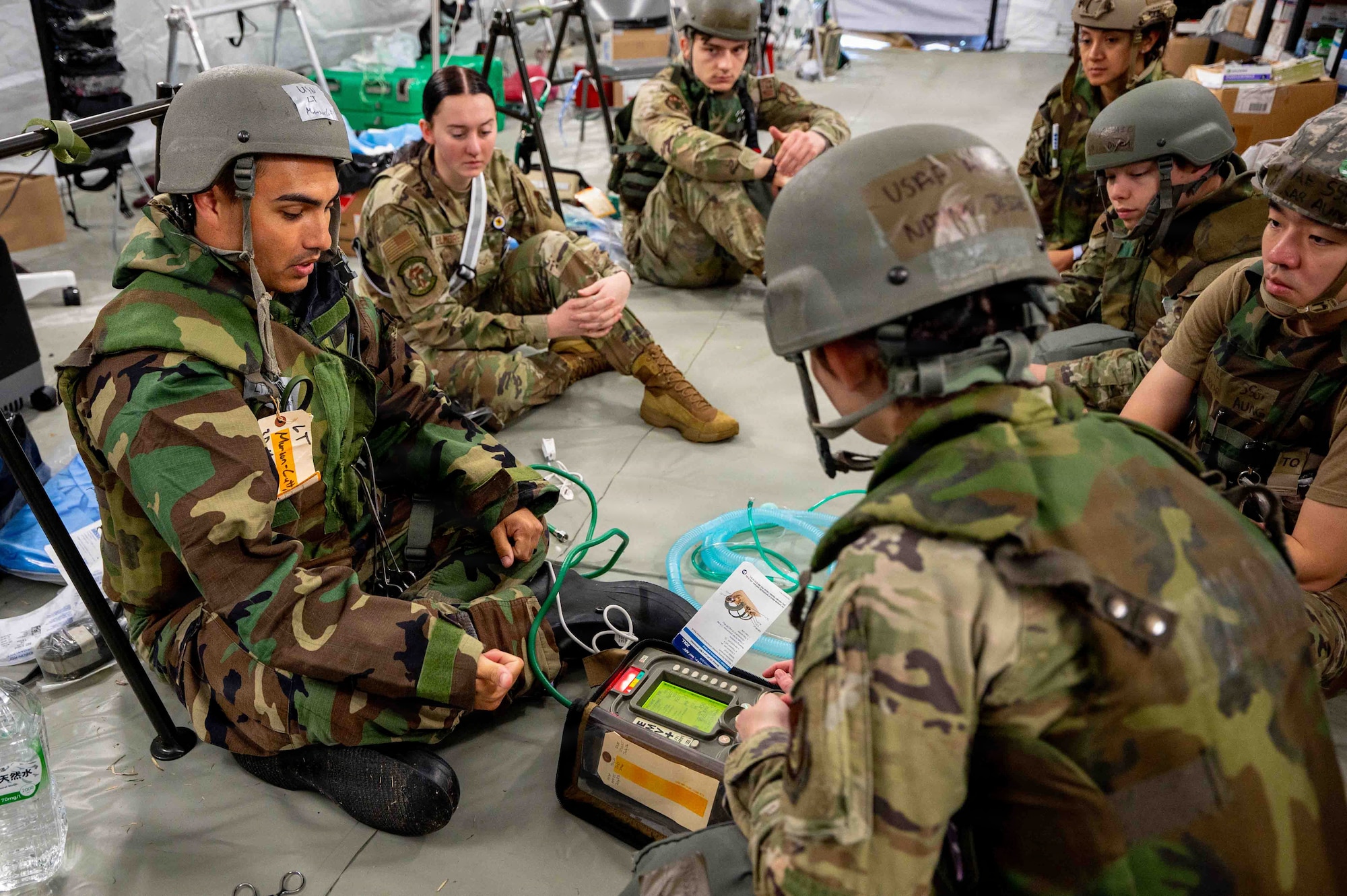 uniformed members sit in a tent on the floor looking at medical equipment