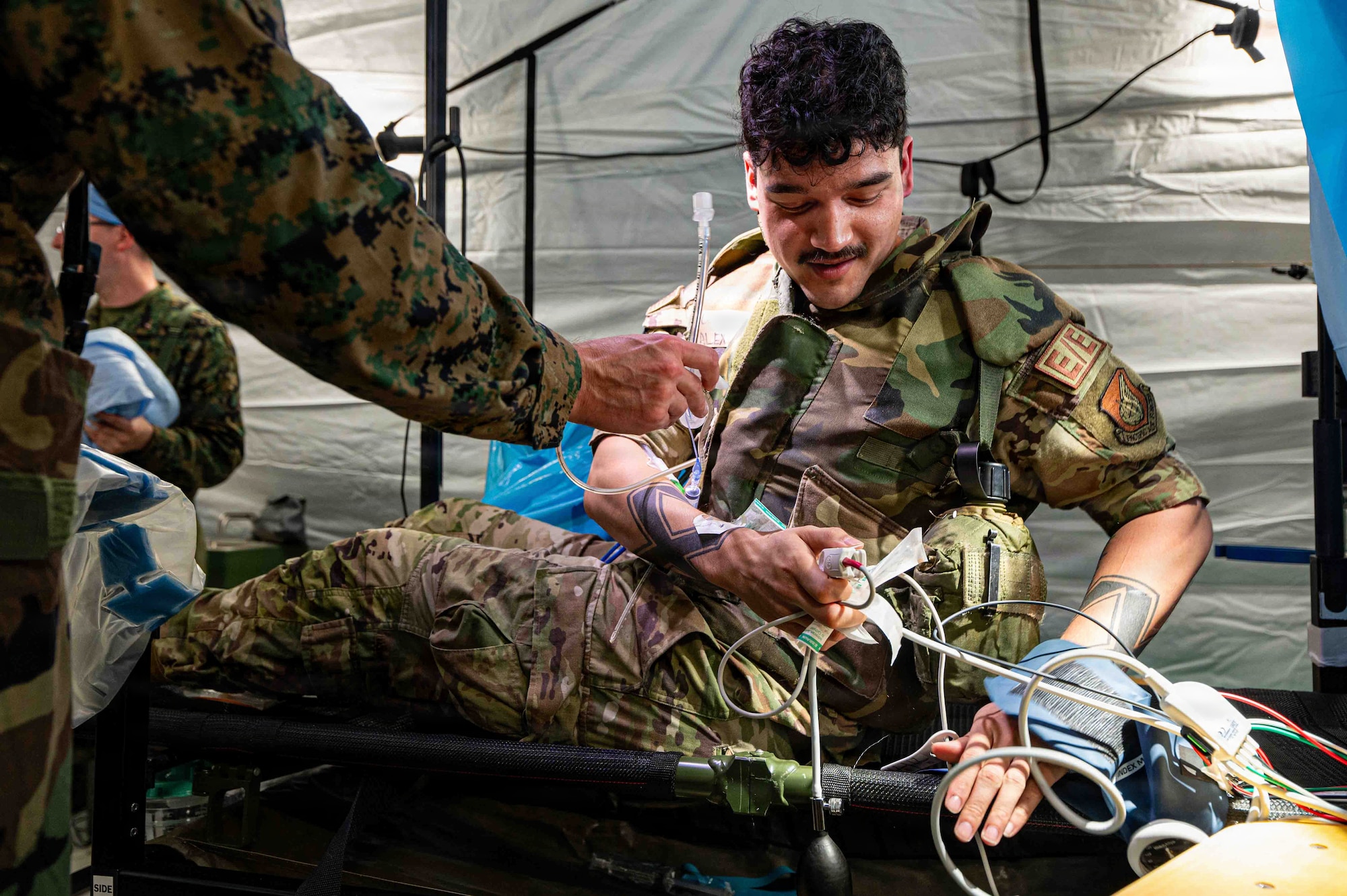 uniformed members sit in a tent on the floor hooked up to tubes and medical equipment