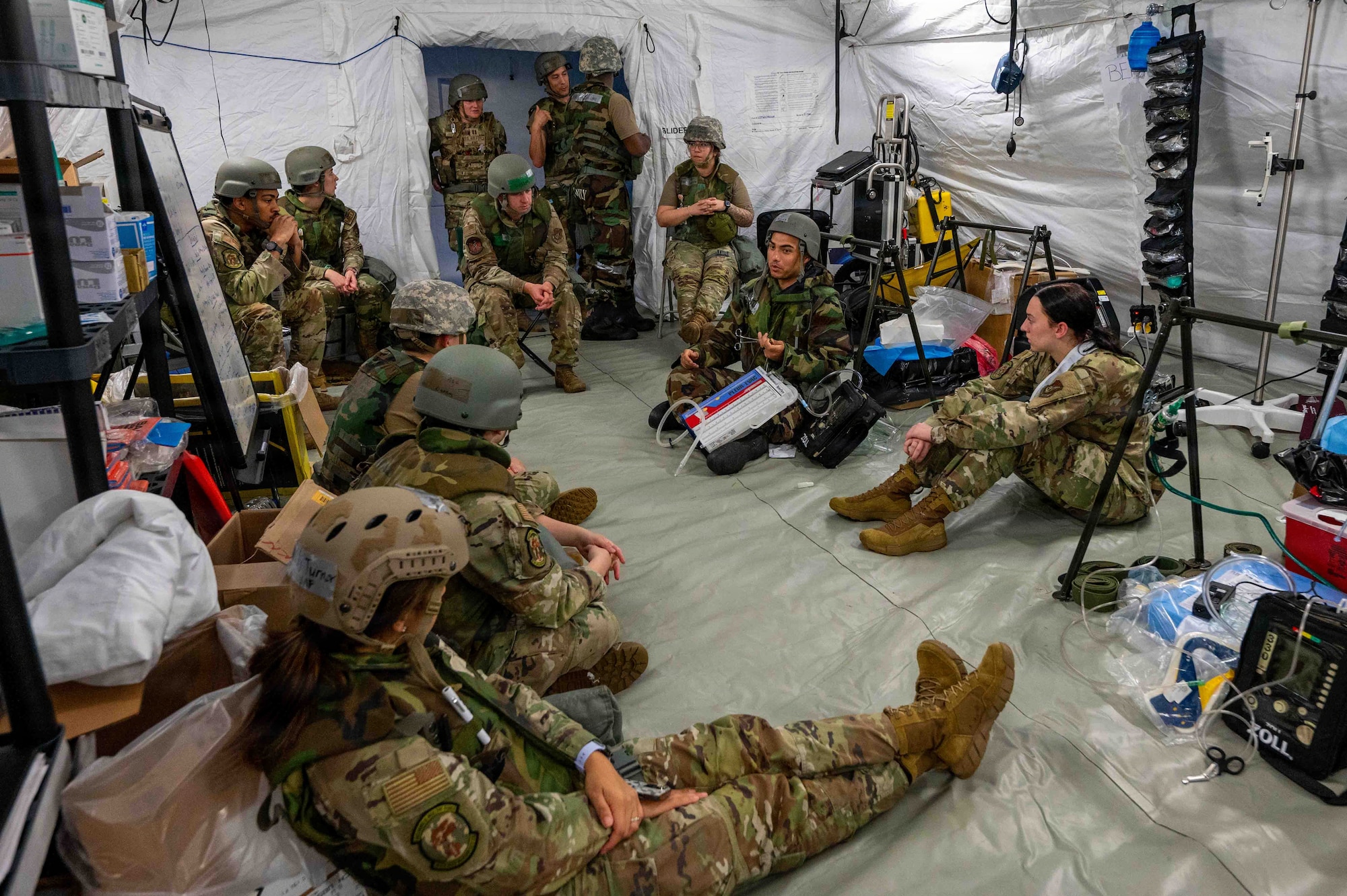 uniformed members wearing protective gear sit in a tent listening to a brief