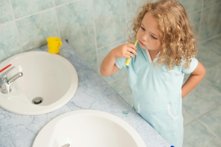 Child stands in front of a bathroom sink and brushes her teeth.