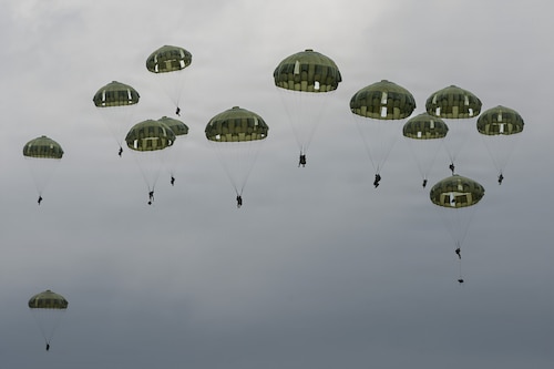 Paratroopers float through the sky.
