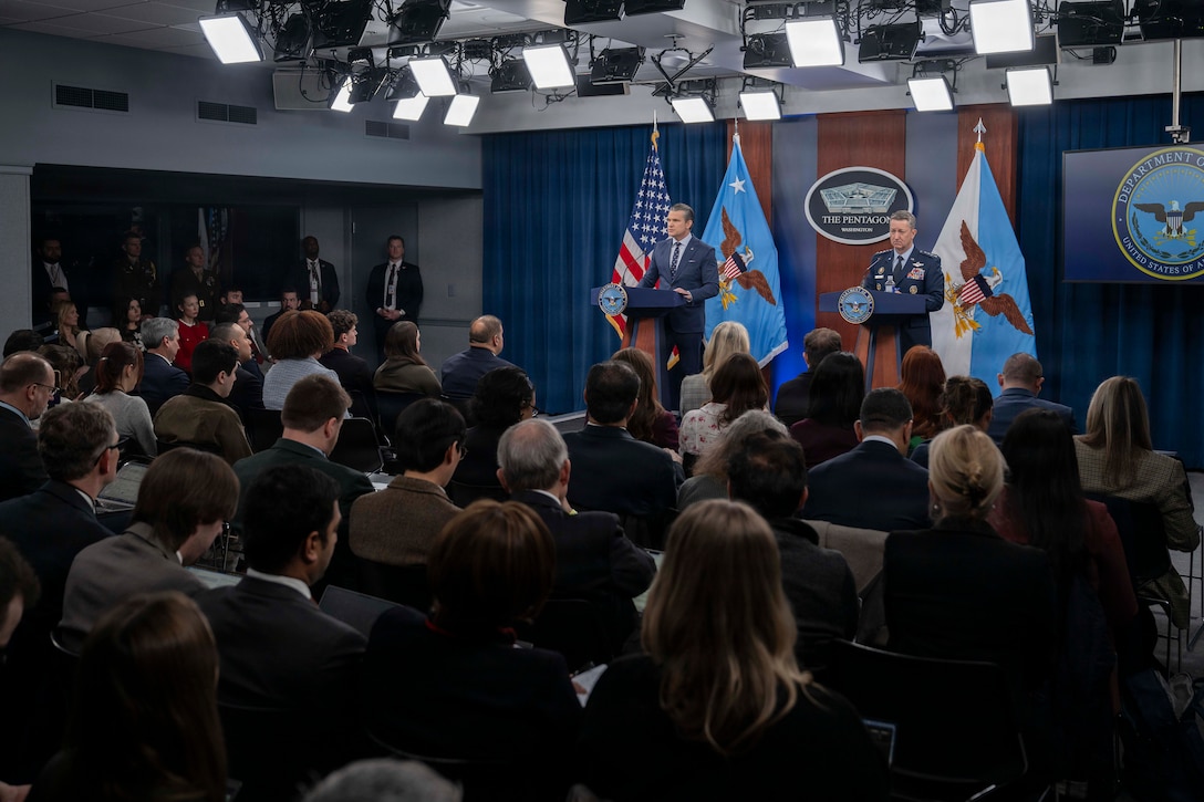 Secretary of War Pete Hegseth and Air Force Gen. Dan Caine speak at lecterns to seated reporters.