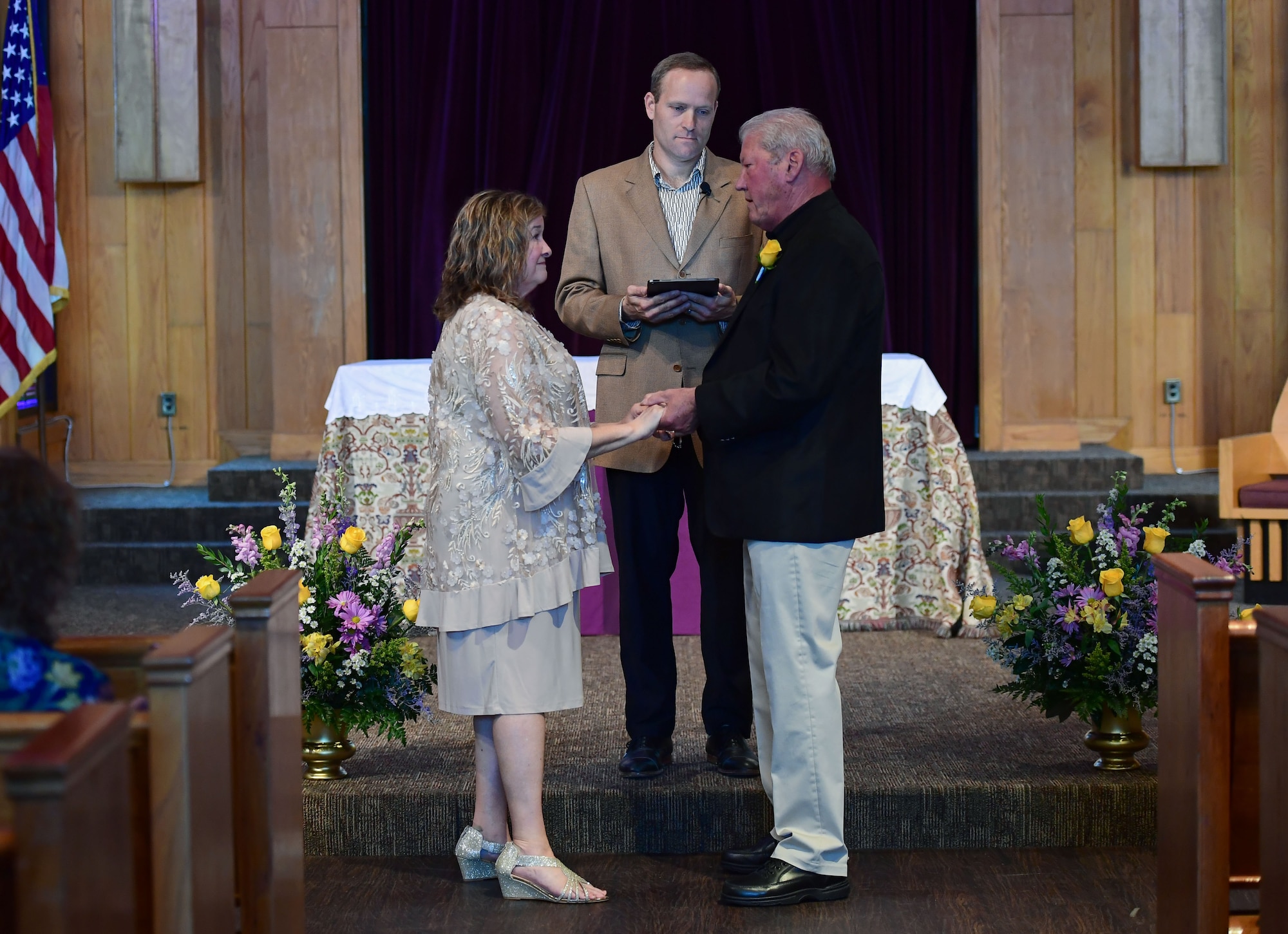 A woman in a dress and a man in slacks and a black dress coat renew their vows in a chapel.