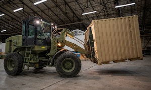An industrial-size forklift moves heavy equipment inside of a cargo bay.