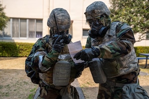 Airmen wearing chemical protective gear use a paper to relay information on a paper.