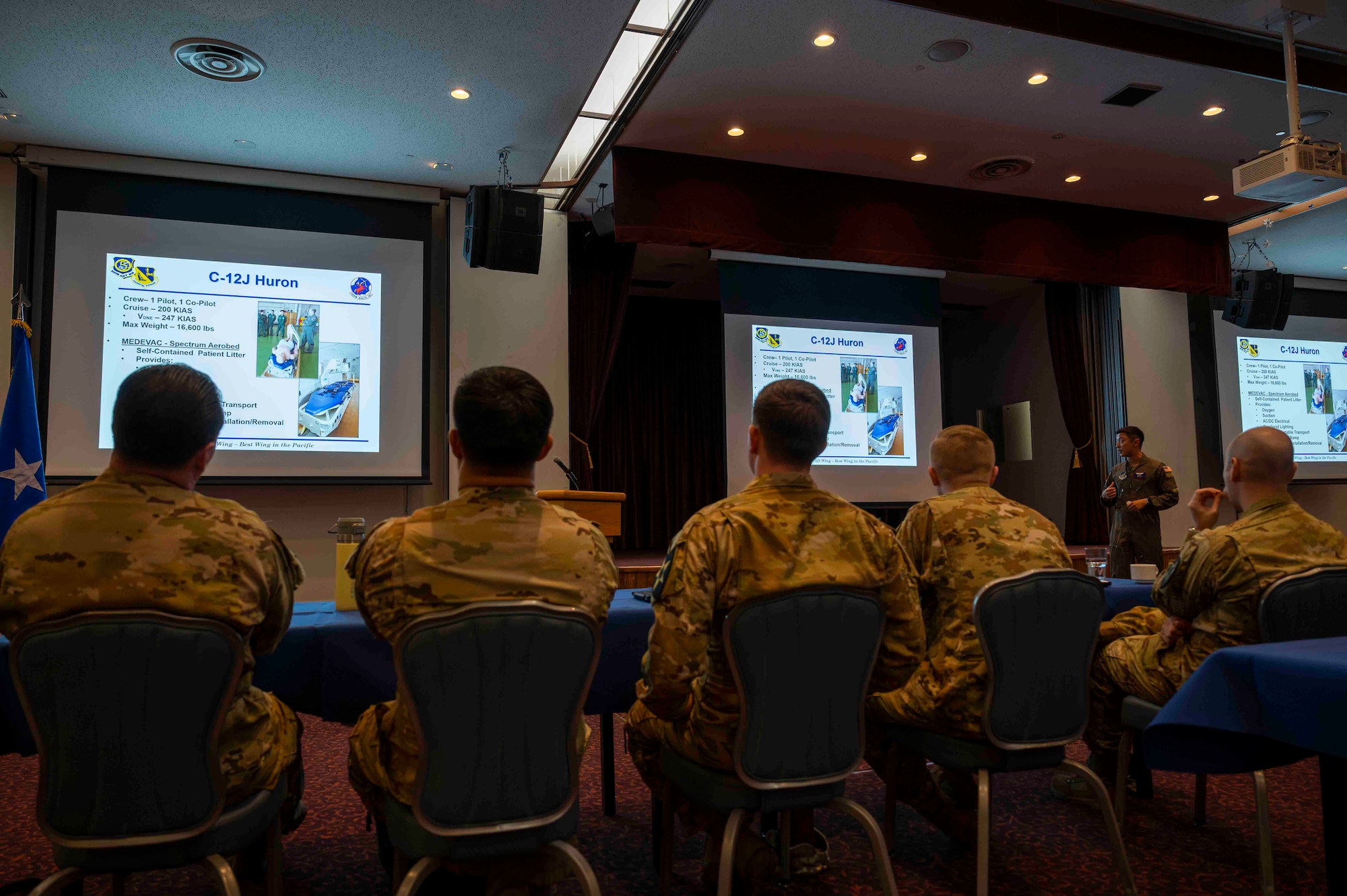 Five military members look at a screen showcasing C-12J Huron capabilities at Yokota.