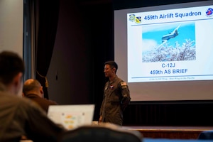 A military member stands in front of a projector showing a C-12J Huron.