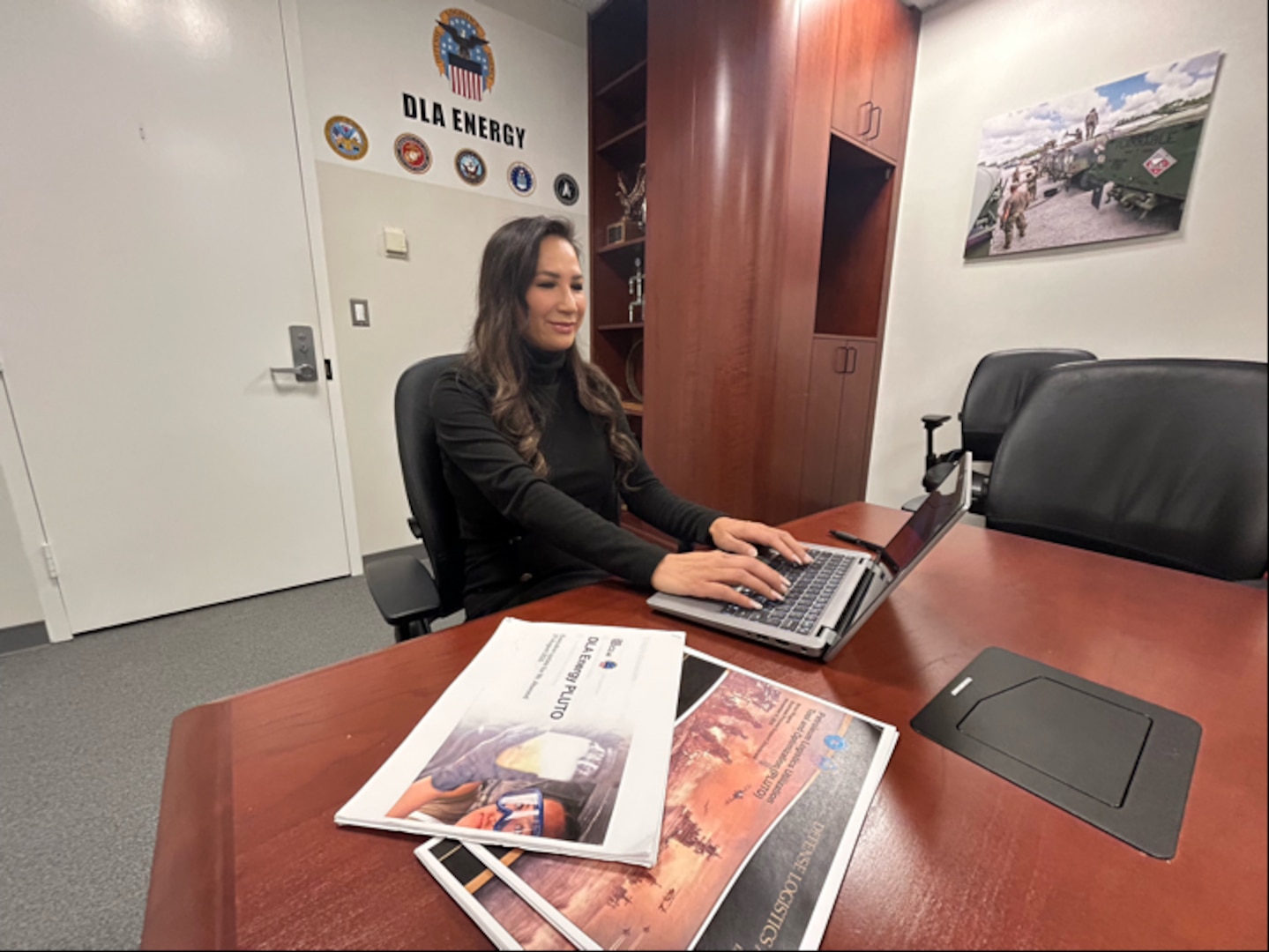 A woman sits at a table in an office and types on a laptop