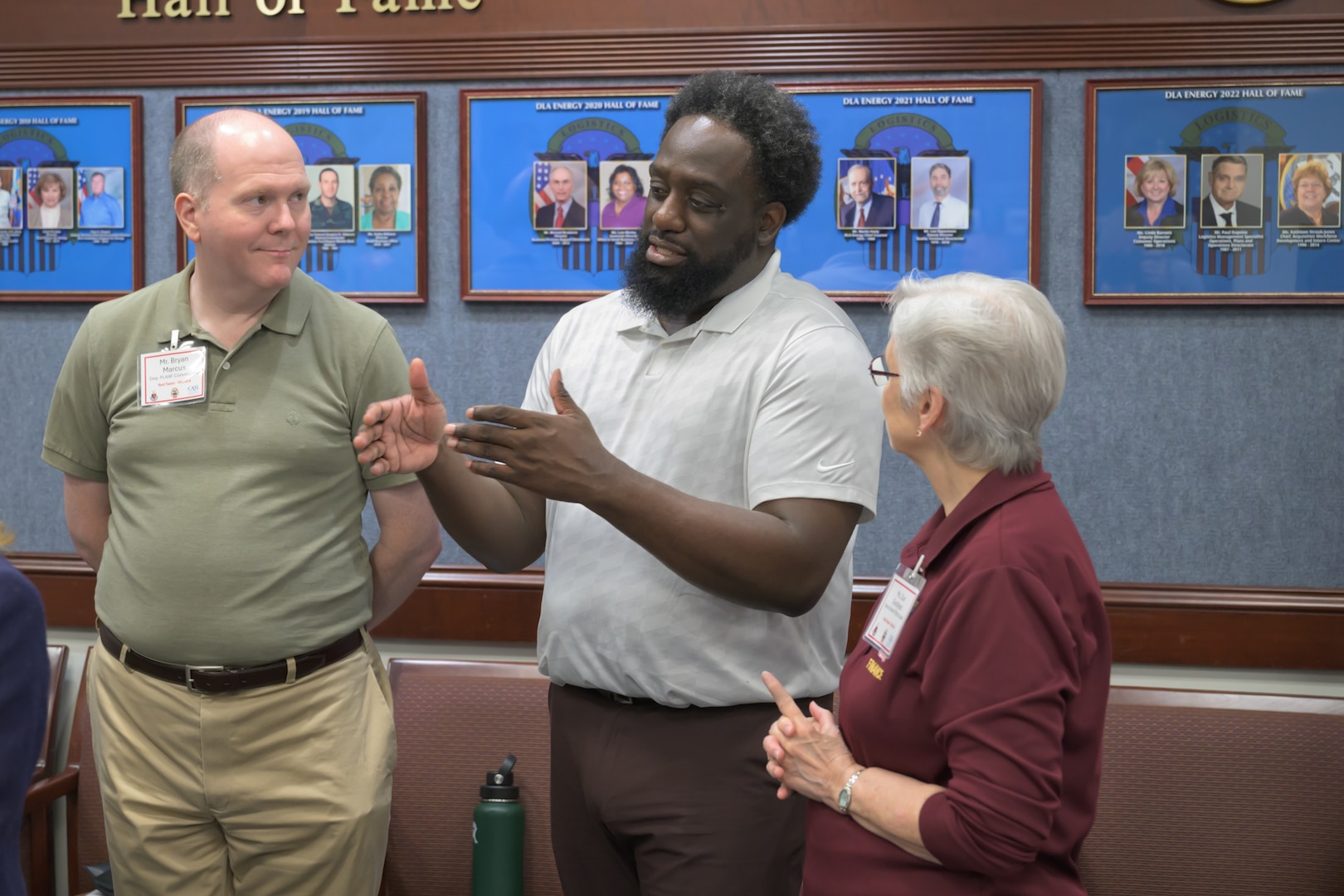 A man stands between two other people, explaining something, using his hands to motion together
