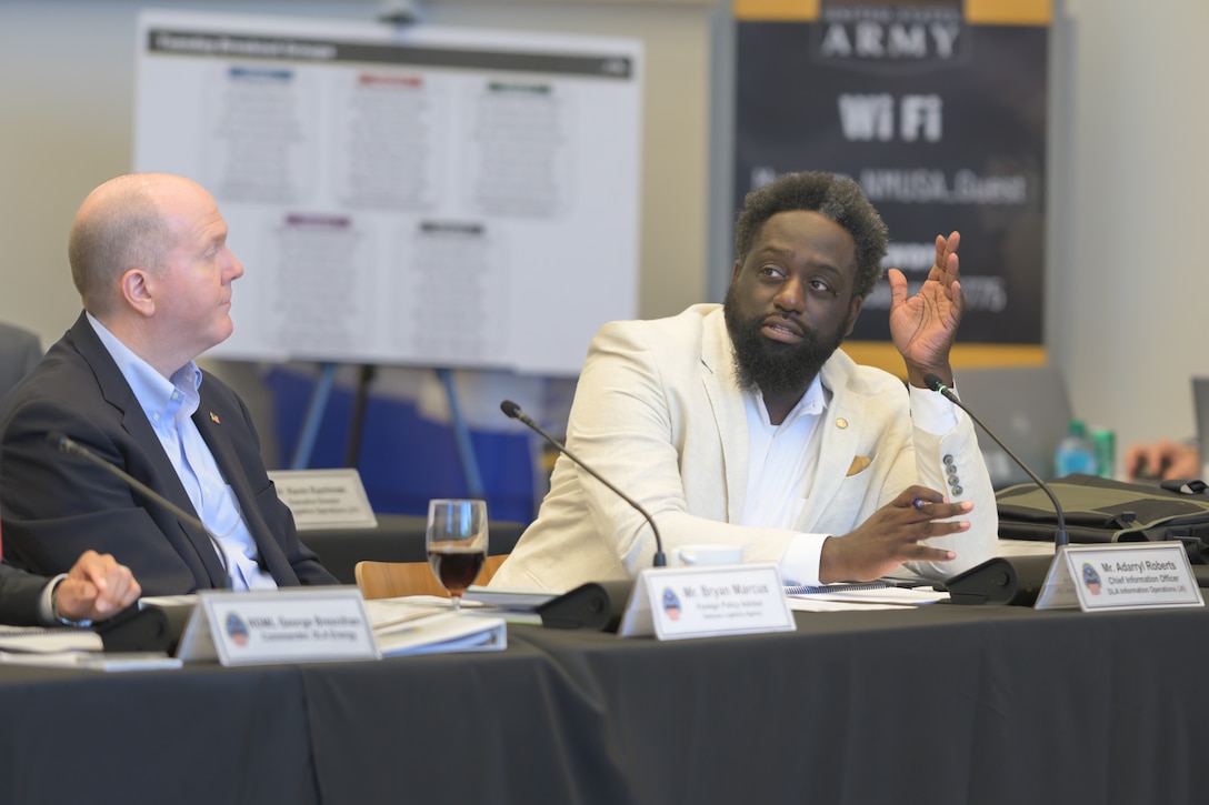 A man in a white suit sits at a panel's table