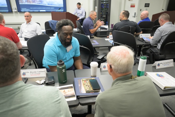 A man in a blue shirt sits across a narrow table from two other men