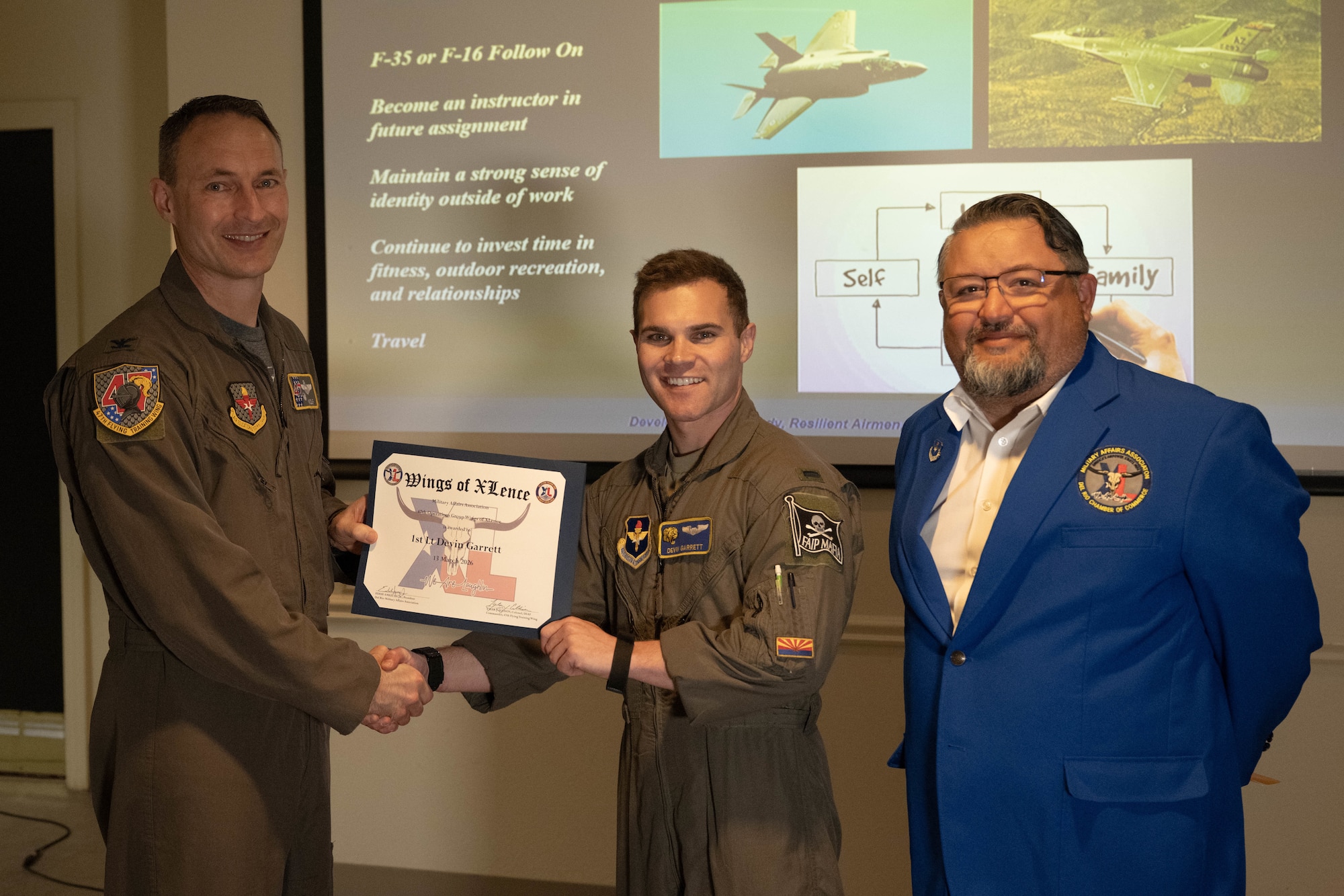 U.S. Air Force Col. Tyler Ellison, 47th Flying Training Wing commander, and Eddie Amezuca, Del Rio Military Affairs Association president, present the Wings of XLence certificate to 1st Lt. Devin Garrett, 85th Flying Training Squadron instructor pilot, at Laughlin Air Force Base, Texas, March 13, 2026. Garrett was recognized as the 47th Operations Group’s top performer throughout the first quarter. (U.S. Air Force photo by Airman 1st Class Darryl Keith)