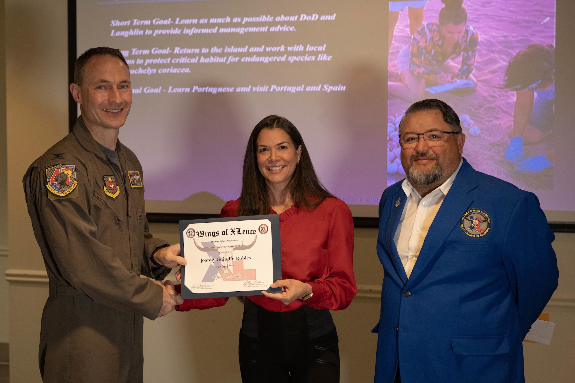 U.S. Air Force Col. Tyler Ellison, 47th Flying Training Wing commander, and Eddie Amezuca, Del Rio Military Affairs Association president, present the Wings of XLence certificate to Joanny Guidin Robles, 47th Civil Engineer Squadron natural resource manager, at Laughlin Air Force Base, Texas, March 13, 2026. Robles was one of five winners acknowledged during the Wings of XLence luncheon. (U.S. Air Force photo by Airman 1st Class Darryl Keith)