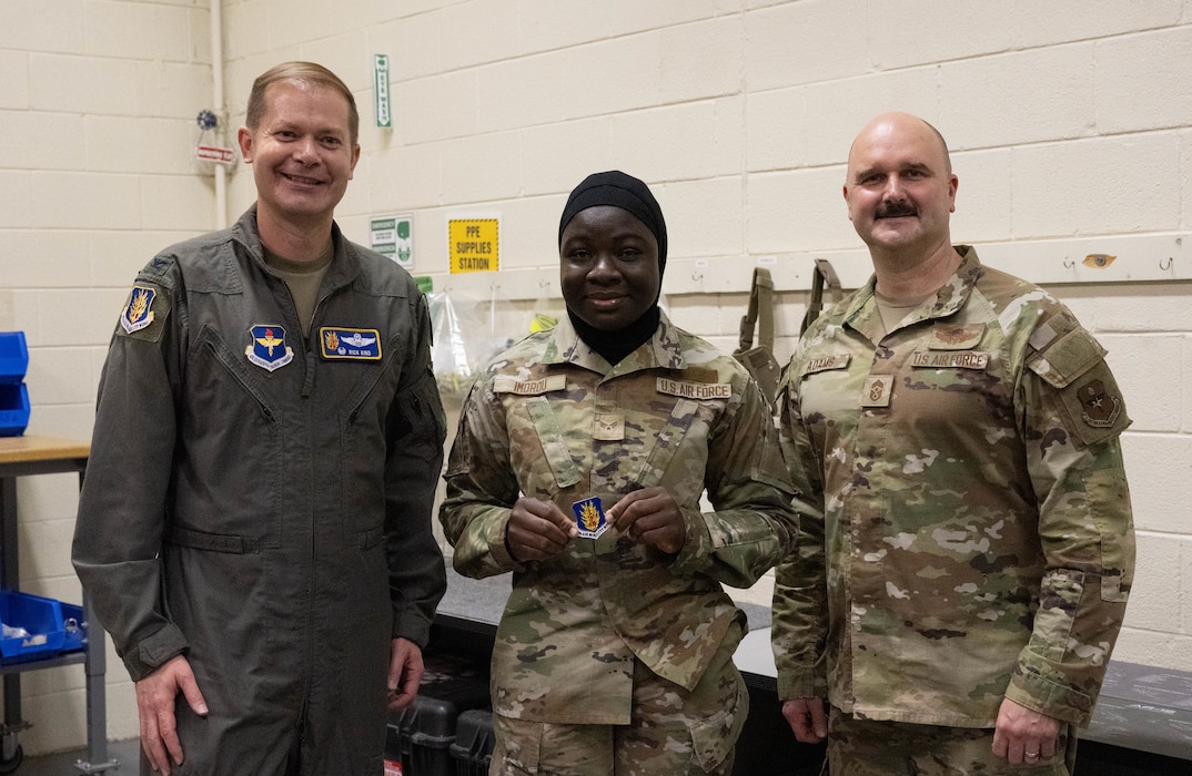 U.S. Air Force Col. Richard Kind, 97th Air Mobility Wing commander, left, and Chief Master Sgt. Jonny Adams, 97th AMW command chief, right, stands with Senior Airman Ouswatoy Mamoudou Imorou, 97th Logistics Readiness Squadron individual protective equipment journeyman, center, as she displays her coin at Altus Air Force Base, Oklahoma, Feb. 25, 2026. Kind recognized Imorou for her outstanding performance, professionalism and dedication to her duties. (U.S. Air Force photo by Airman 1st Class Emma Wright)
